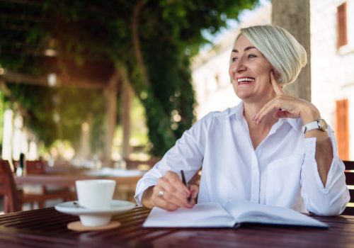 Happy senior woman writing to notebook or diary at a cafe